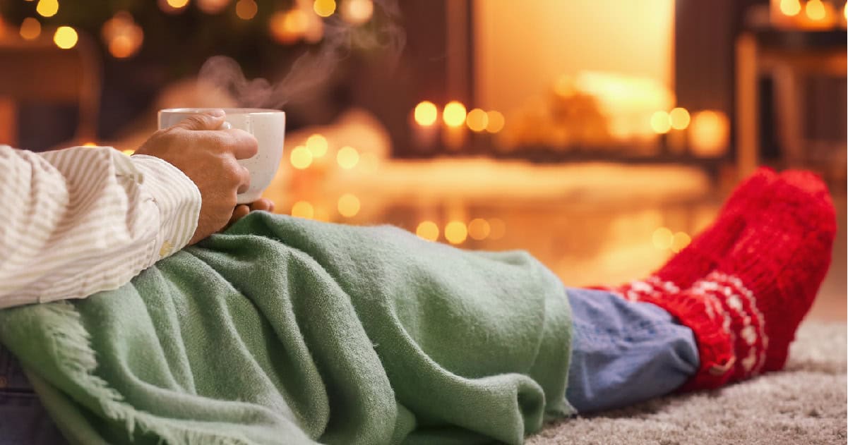 person relaxing with a cup of tea in front of the fireplace